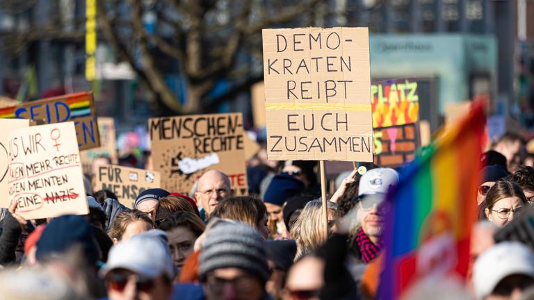 Bei einer Demonstration ist auf einem Plakat der Schriftzug "Demokraten reißt euch zusammen" zu sehen.