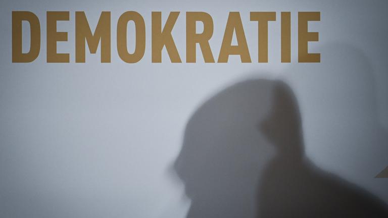 Berlin: Ein doppelter Schatten ist unter dem Schriftzug "Demokratie" zu sehen.