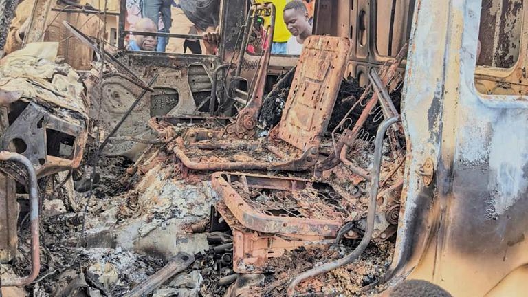 Menschen versammeln sich um die verkohlten Überreste eines verbrannten Fahrzeugs.