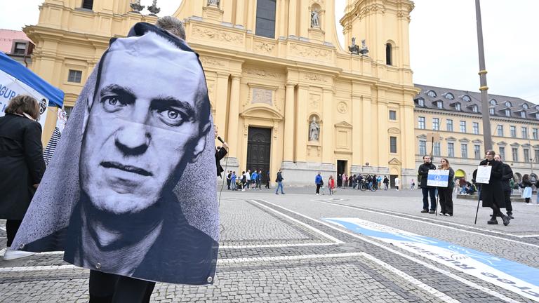 Bayern, München: Ein Demonstrant trägt einen Umhang mit einem Bild von Alexej Nawalny