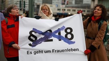 Demonstranten halten ein Transparent hoch, auf dem eine durchgestrichene Nummer des Paragraphen 218 zu sehen ist