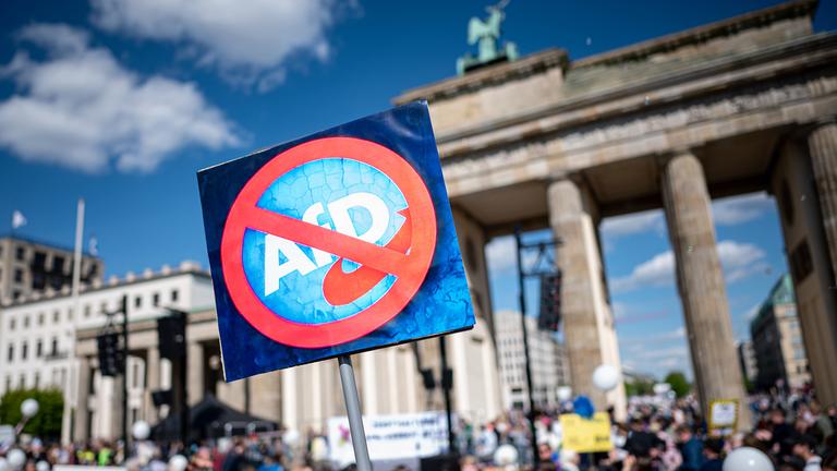 Eine Person hält am bundesweiten Aktionstag "Keine Ausreden mehr - AfD-Verbot jetzt!" am Brandenburger Tor ein Schild mit einem durchgestrichenen Logo der AfD