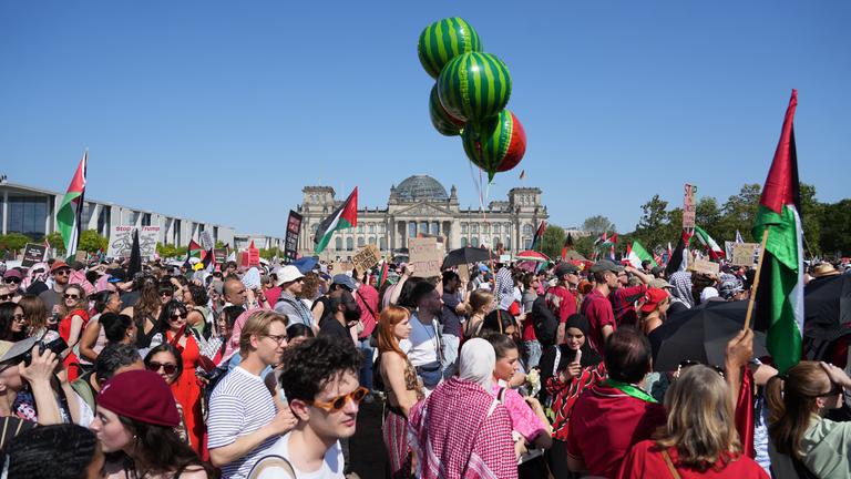 Viele protestierende Menschen, unteranderem mit palästinischen Flaggen. Im Hintergrund ist das Reichstagsgebäude.