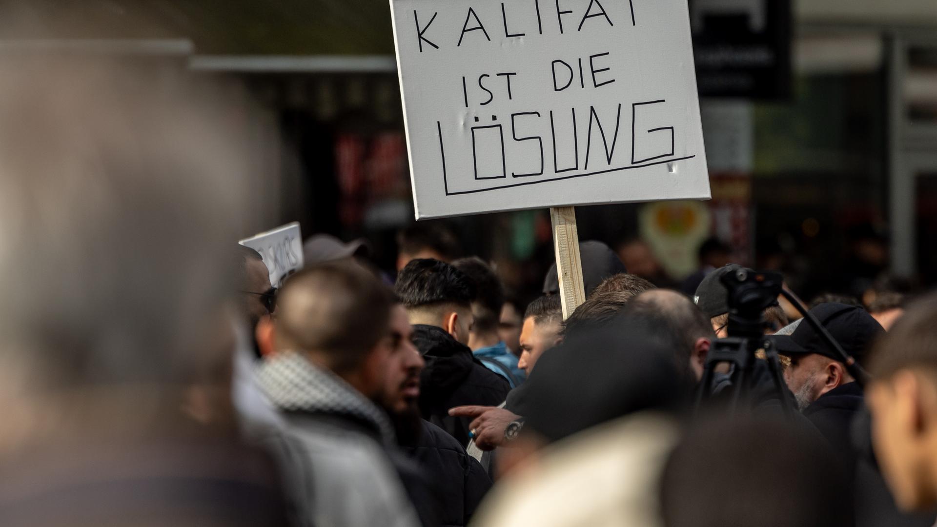 Teilnehmer einer Islamisten-Demo halten ein Plakat mit der Aufschrift "Kalifat ist die Lösung" in die Höhe. Am 27.04.2024 in Hamburg