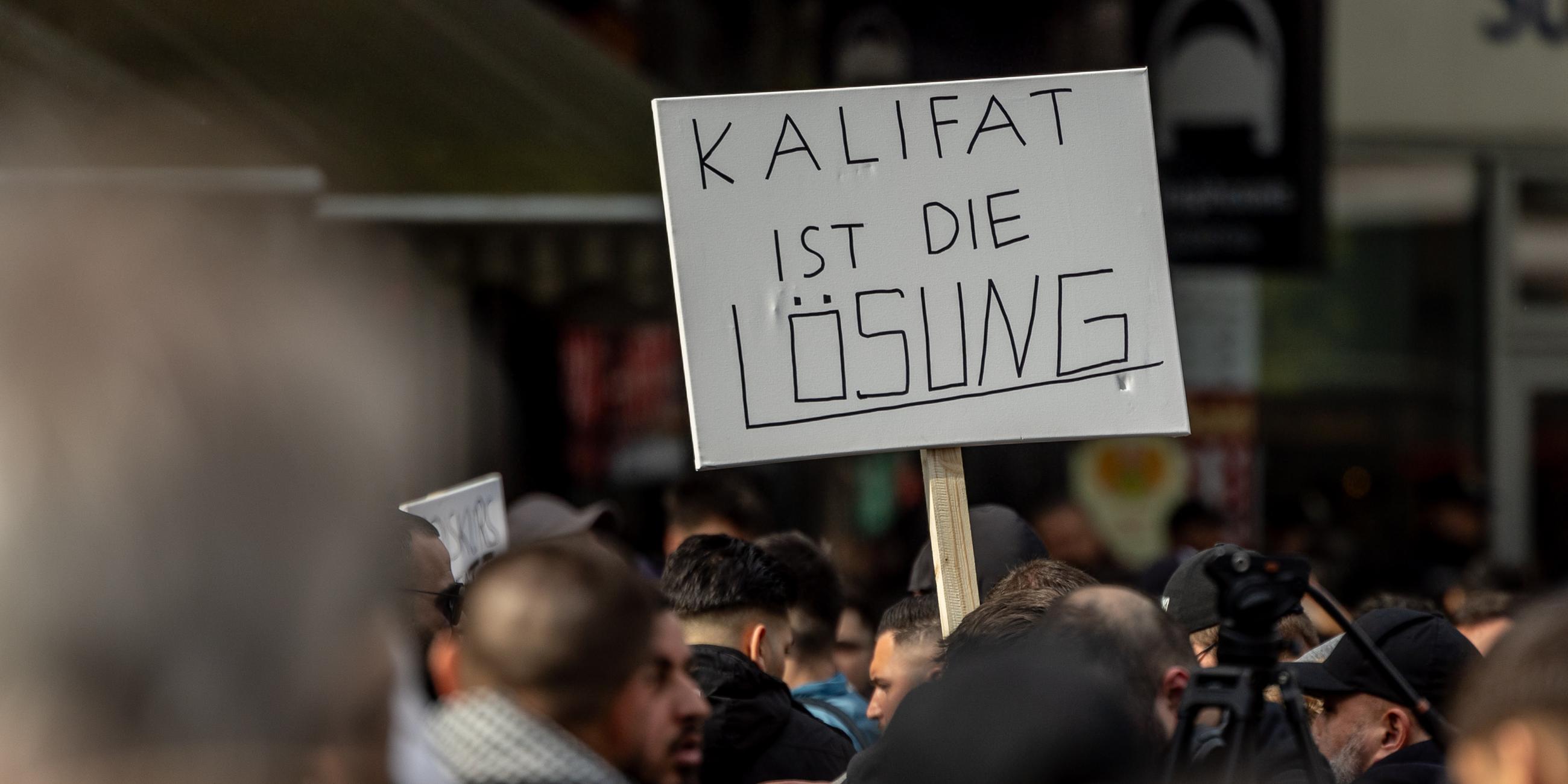Teilnehmer einer Islamisten-Demo halten ein Plakat mit der Aufschrift "Kalifat ist die Lösung" in die Höhe. Am 27.04.2024 in Hamburg