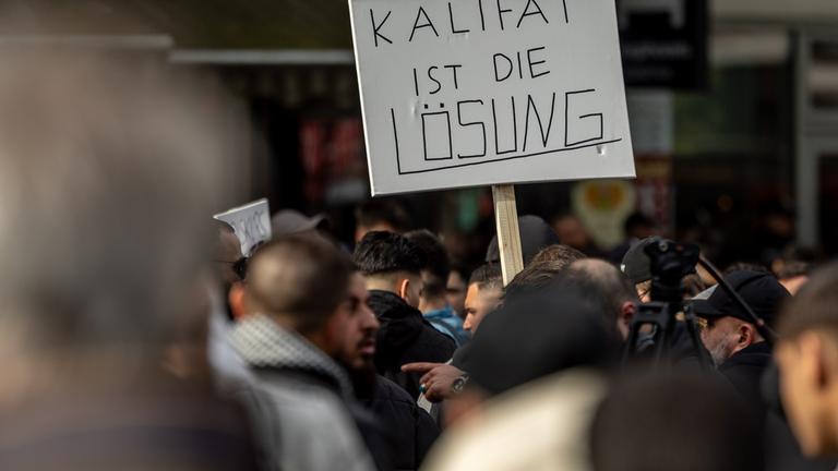 Teilnehmer einer Islamisten-Demo halten ein Plakat mit der Aufschrift "Kalifat ist die Lösung" in die Höhe. Am 27.04.2024 in Hamburg