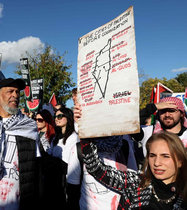 Eine Frau hält bei einer pro-palästinensischen Demonstration unter dem Motto „United4Palestine“  in Berlin ein Plakate hoch. Hinter ihr stehen weitere Demonstranten. 