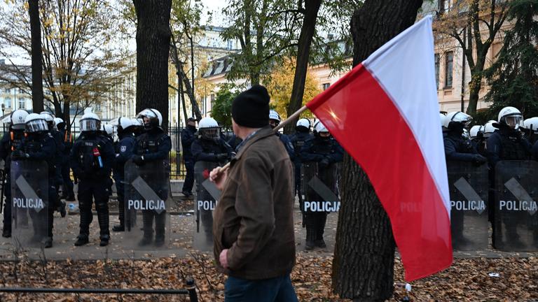 Ein Demonstrant läuft mit der polnische Nationalflagge am 31.10.2026 in Warschau, Polen, an Polizisten vorbei.