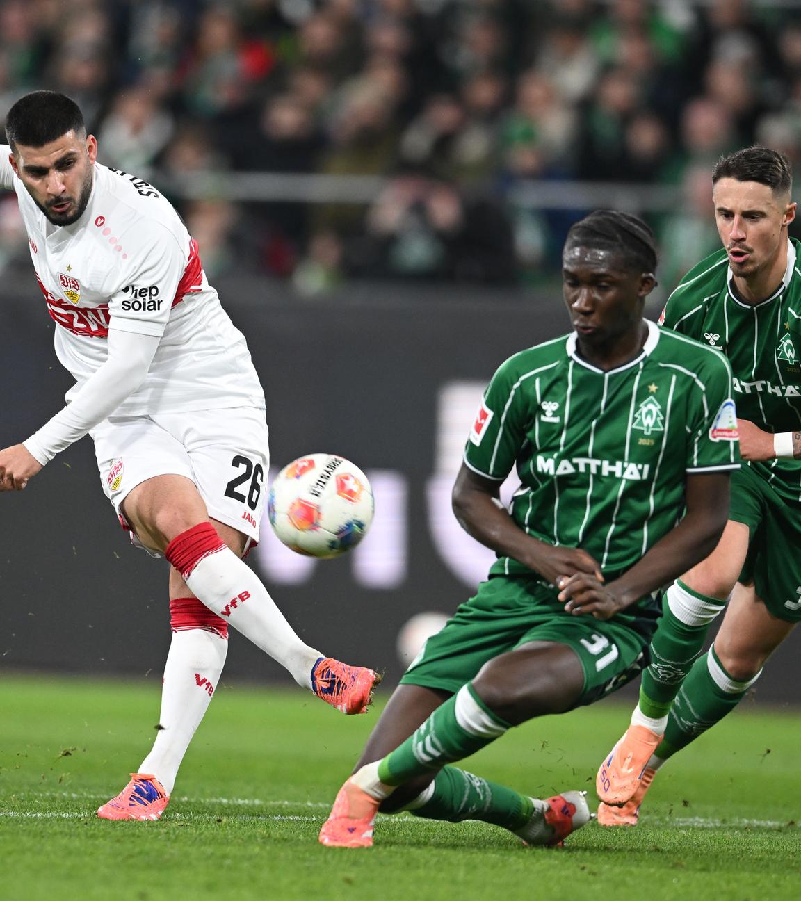 Stuttgarts Stürmer Deniz Undav schießt den Ball in Richtung des Bremer Tors, wird dabei jedoch von Bremens Karim Coulibaly und Marco Friedl bedrängt.