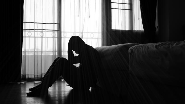 Ein Mann sitzt im Schatten auf dem Boden und stützt seinen Kopf mit seinen Händen. Bei einer Depression ist einem alles zu viel.