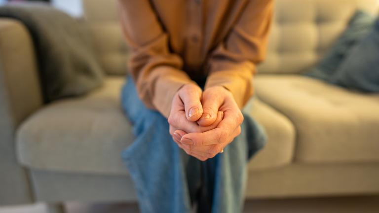 Nahaufnahme einer Frau, die nervös die Hände verschränkt und ängstlich auf der Couch auf Neuigkeiten wartet. Angst und psychisch