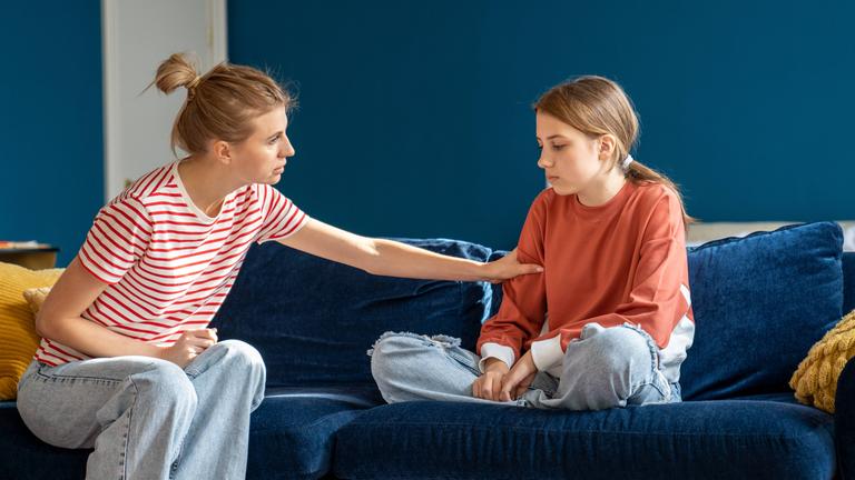 Mutter und Tochter sitzen uaf dem Sofa. Die Mutter versucht, mit ihrer traurigen und depressiven Tochter zu sprechen.
