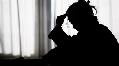 Niedersachsen, Hannover: Die Silhouette einer Frau zeichnet sich vor einer hellen Fensterfront ab (gestellte Szene).