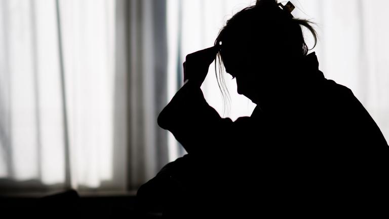 Niedersachsen, Hannover: Die Silhouette einer Frau zeichnet sich vor einer hellen Fensterfront ab (gestellte Szene).