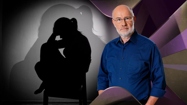 Harald Lesch steht neben trauriger Frau auf Stuhl