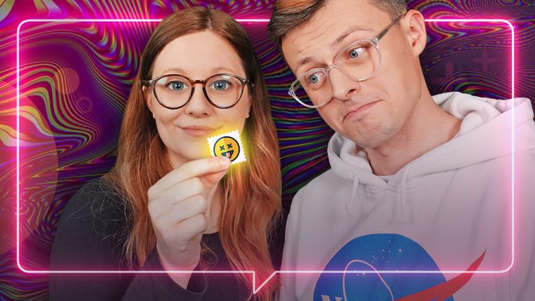 Leonie und Jacob stehen vor einem regenbogenfarbenen Hintergrund. Leonie hat weit geweitete Pupillen und sieht in die Kamera. Jacob neigt sich fragend zu Leonie und sieht verdutzt auf die Pille, die Leonie in der Hand hat.