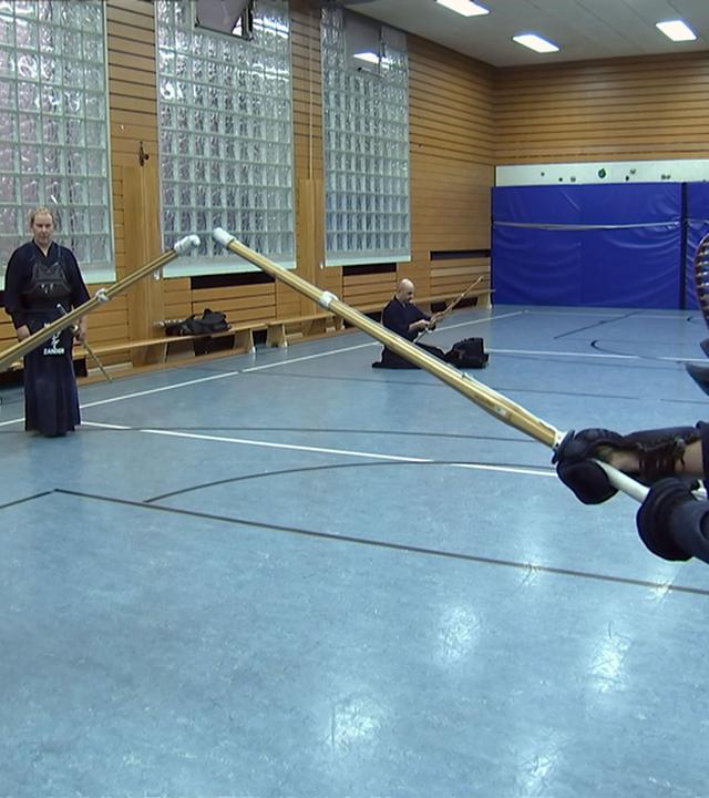 Zwei Kendo-Kämpfer treten in einer Turnhalle gegeneinander an.