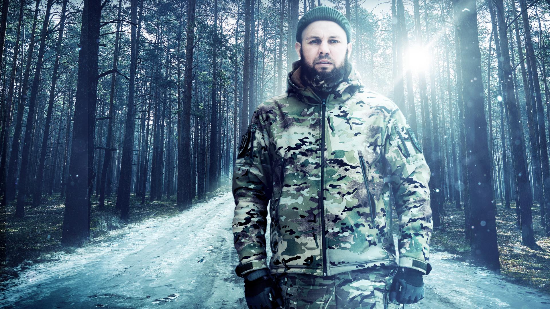 Gegenlichtaufnahme: Ein Soldat steht in einem Wald und schaut in die Kamera.