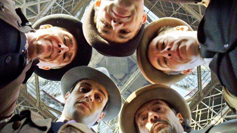 Fünf Männer mit Hut stecken die Köpfe zusammen