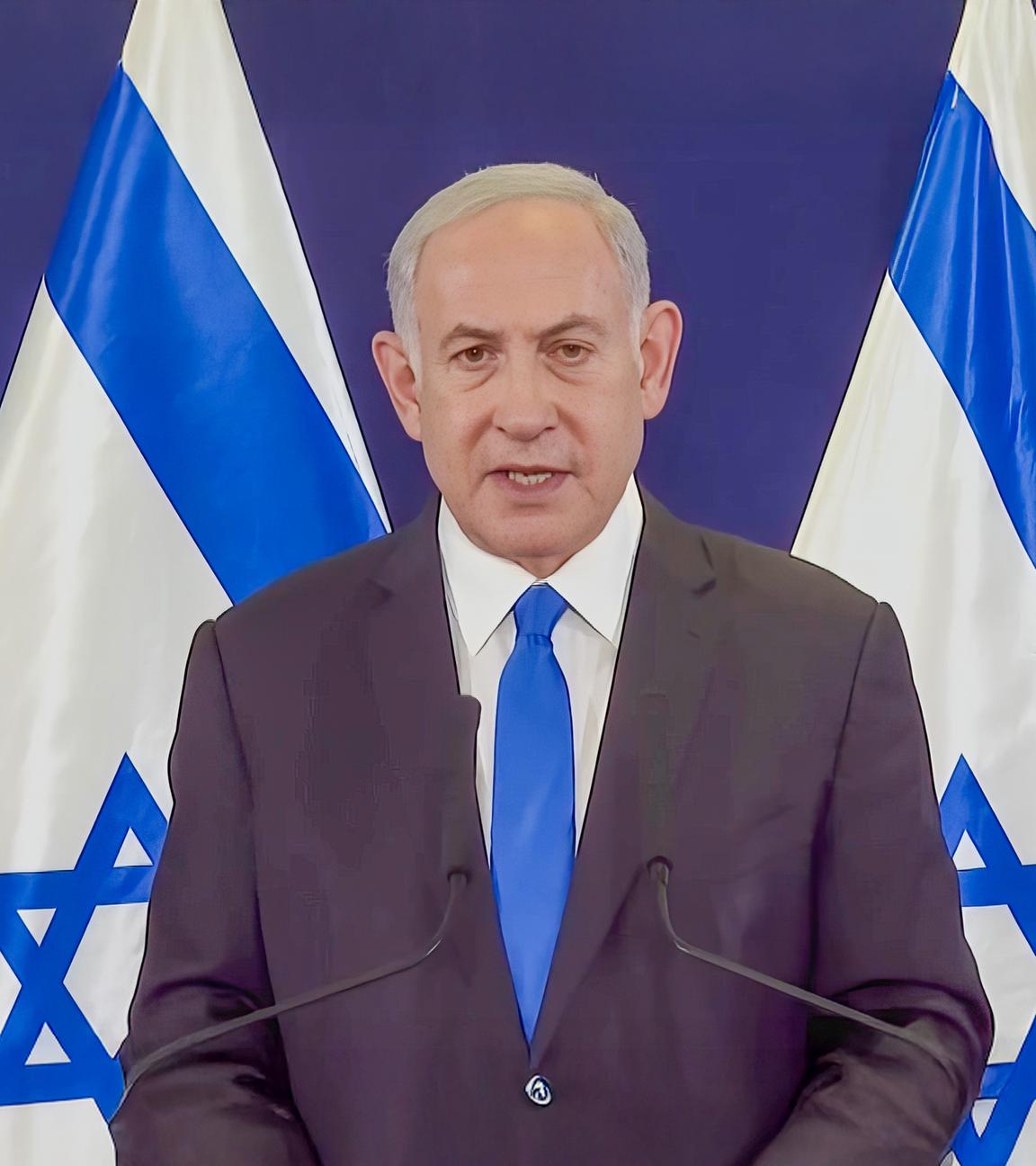 Der israelische Premierminister Benjamin Netanjahu steht bei einem Presseauftritt vor vier israelischen Flaggen.