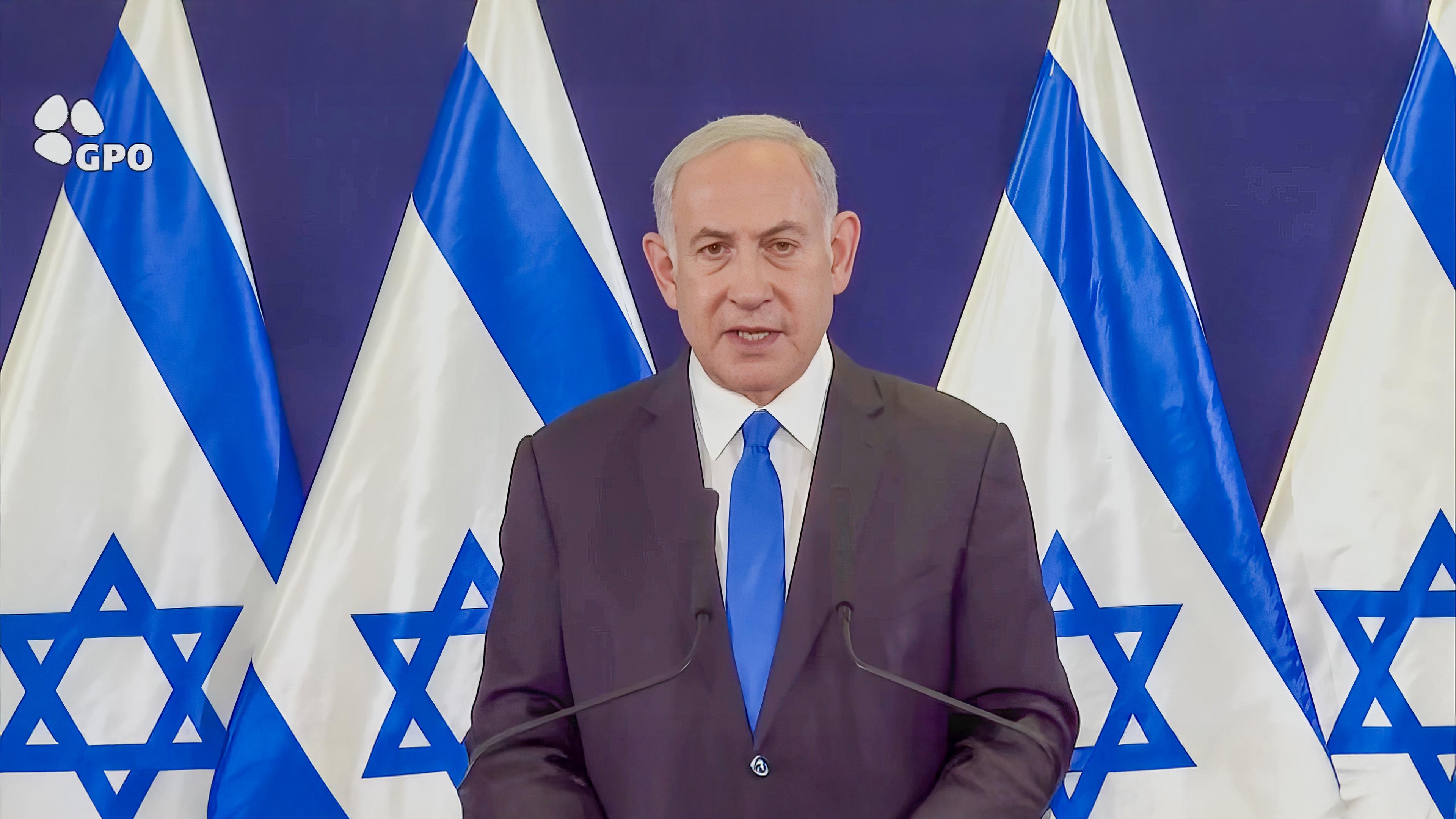 Der israelische Premierminister Benjamin Netanjahu steht bei einem Presseauftritt vor vier israelischen Flaggen.