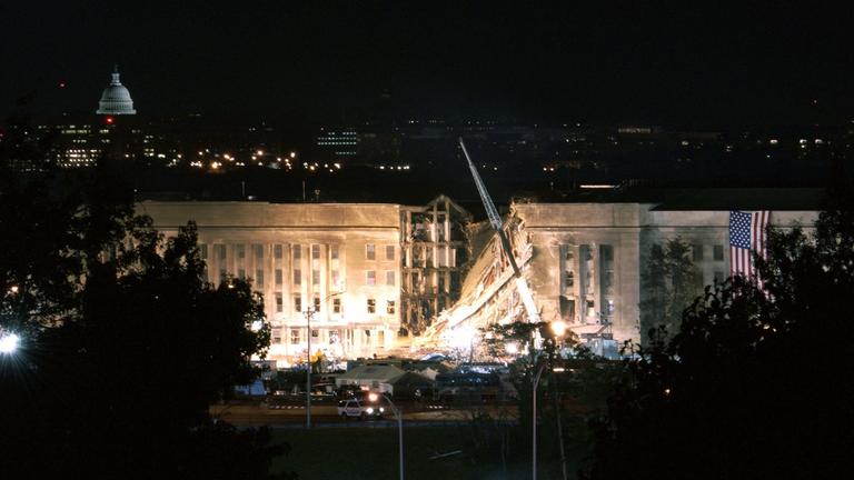"Der Preis des Krieges: Kampf gegen den Terror": Blick auf das, durch einen Terroranschlag beschädigte, Pentagon bei Nacht. Das Gebäude wird angestrahlt. Links hängt eine US-Flagge am Gebäude.