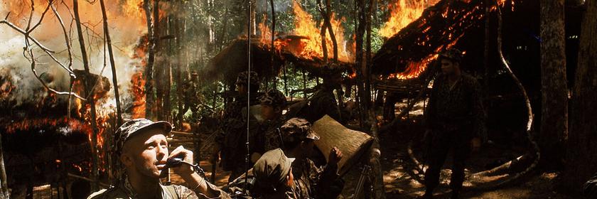 "Der Preis des Krieges - Vietnam": Ein US-Soldat telefoniert via Funk in einem Wald, umgeben von brennenden Hütten. Um ihn herum stehen weitere Soldaten.