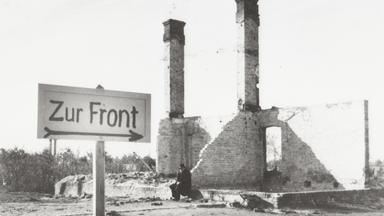 "Der Zweite Weltkrieg: Der Überfall": Ein Mann sitzt in den Ruinen eines durch den Krieg zerstörten Hauses in einer polnischen Ortschaft. Im Vordergrund ist ein Wegweiser mit der Aufschrift "Zur Front" errichtet worden.