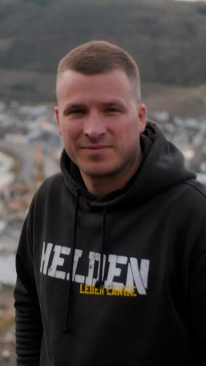 Ein junger Mann in einem schwarzen Kapuzenpullover steht auf einem Aussichtspunkt über Dernau, einem Ort im Ahrtal.