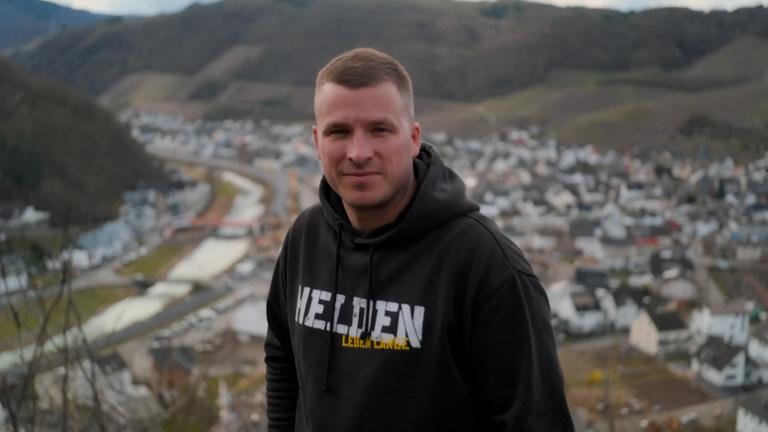 Ein junger Mann in einem schwarzen Kapuzenpullover steht auf einem Aussichtspunkt über Dernau, einem Ort im Ahrtal.