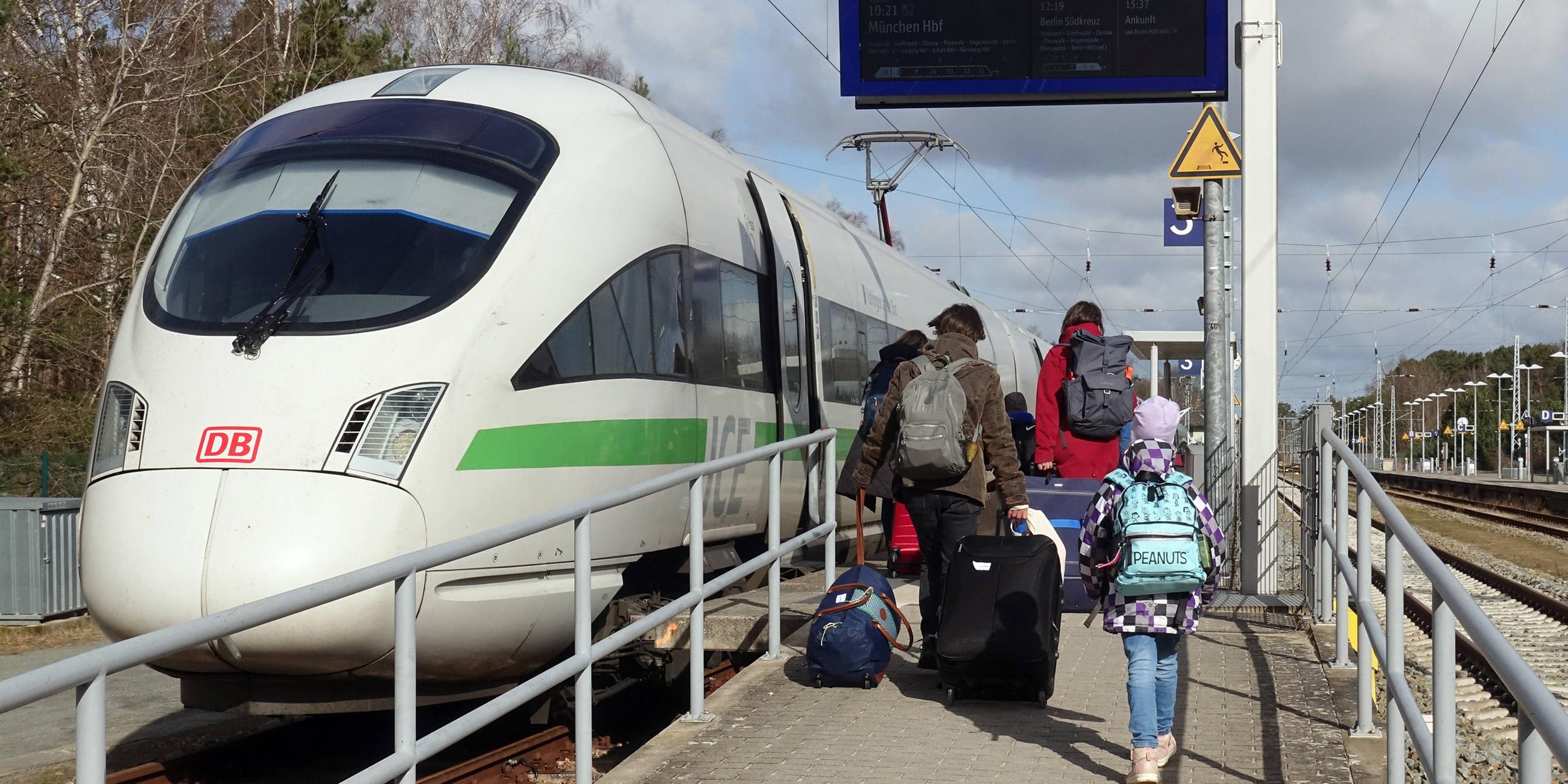 Eine Familie läuft an einem Bahngleis an dem ein ICE wartet.