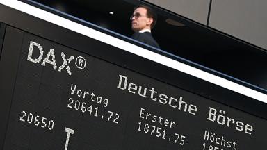 Während ein Besucher auf der Empore der Frankfurter Wertpapierbörse steht, zeigt die Anzeigetafel mit der Dax-Kurve einen starken Verlust an. 