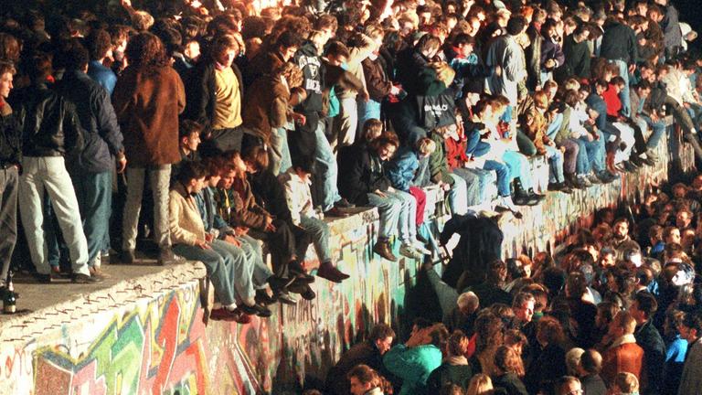 Jubelnde Menschen mit Wunderkerzen sitzen auf der Berliner Mauer am 11. November 1989 nach der Öffnung der innerdeutschen Grenze.