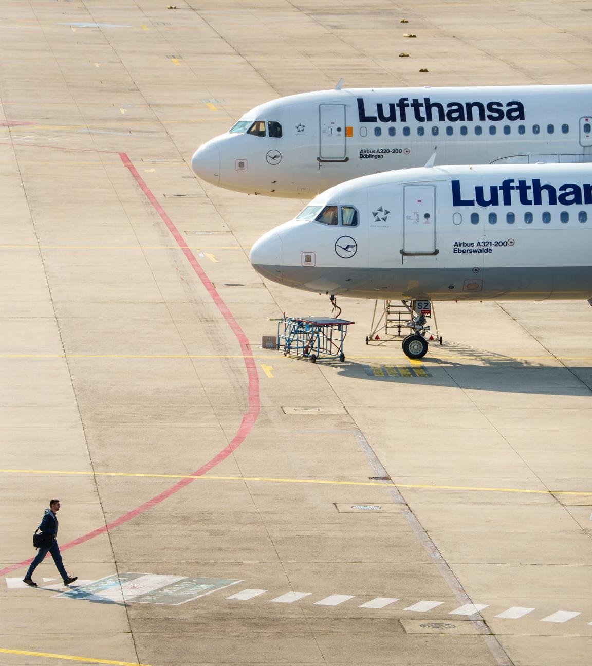 Ein Mann geht an zwei Lufthansamaschinen vorbei