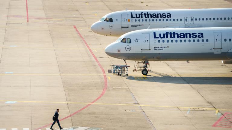 Ein Mann geht an zwei Lufthansamaschinen vorbei