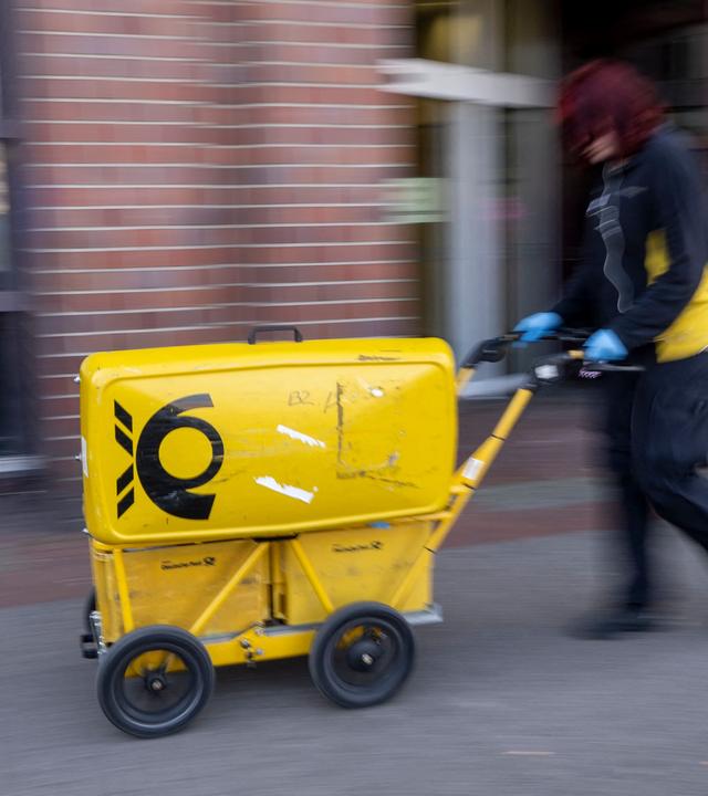 Ein Mitarbeiter der Deutschen Post schiebt einen Postwagen.