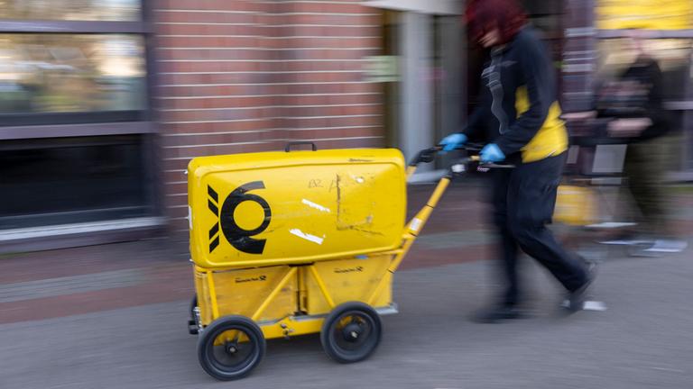 Ein Mitarbeiter der Deutschen Post schiebt einen Postwagen.
