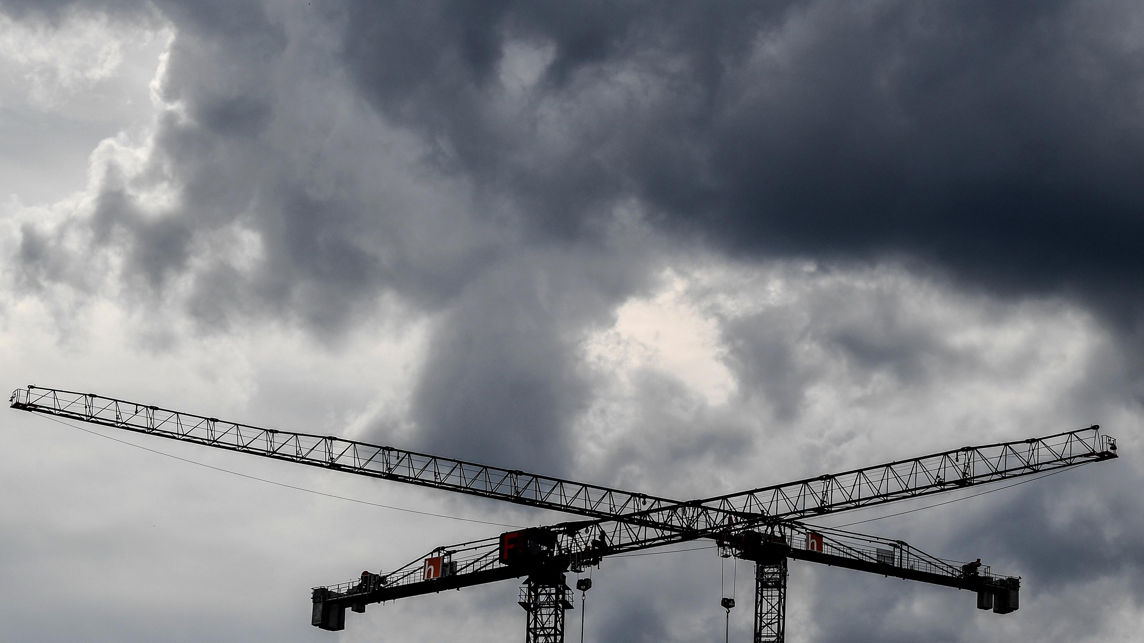 Symbolbild: Baukräne sind vor dunklen Wolken zu sehen. 