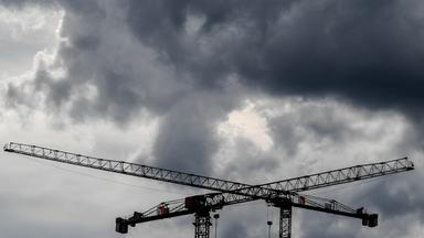 Symbolbild: Baukräne sind vor dunklen Wolken zu sehen. 