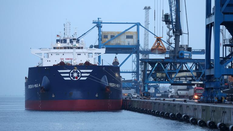 Mecklenburg-Vorpommern, Rostock: Im Überseehafen an der Ostsee liegt am Morgen ein Frachter zur Abfertigung an einem Kai, während Hafenkräne im Hintergrund für den Umschlag von Gütern bereitstehen.