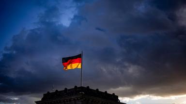 Die deutsche Flagge auf einem Gebäude vor dem Hintergrund dunkler Wolken.