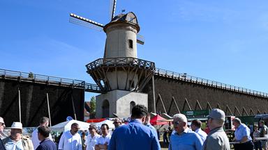 Menschen stehen vor einer Mühle bei blauem Himmel und Sonnenschein.