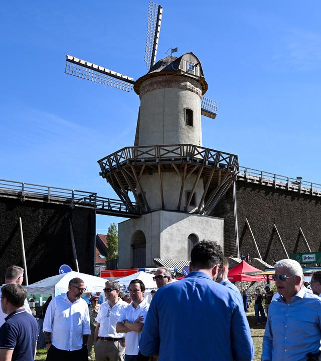 Menschen stehen vor einer Mühle bei blauem Himmel und Sonnenschein.