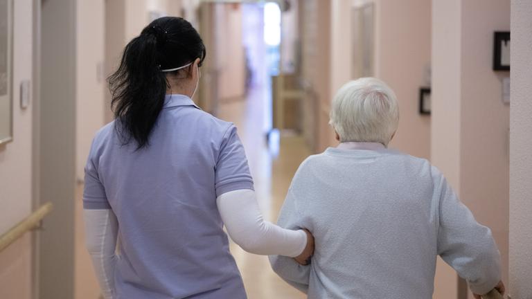 Pflegerin läuft mit älterer Frau einen Krankenhausgang entlang. Frankfurt, Hessen. 