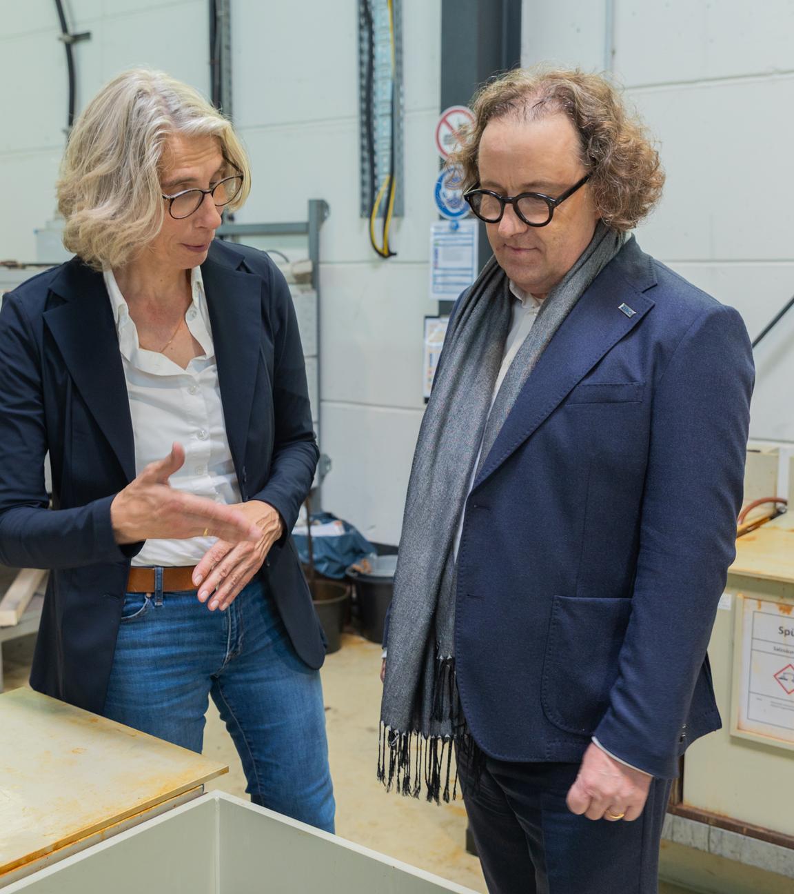 Das Geschäftsführungsduo des Stahlverzinkungsunternehmens Zinq, Birgitt Bendiek und Lars Baumgürtel steht in einer Werkshalle.