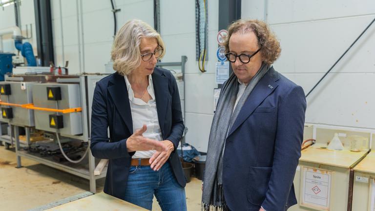 Das Geschäftsführungsduo des Stahlverzinkungsunternehmens Zinq, Birgitt Bendiek und Lars Baumgürtel steht in einer Werkshalle.