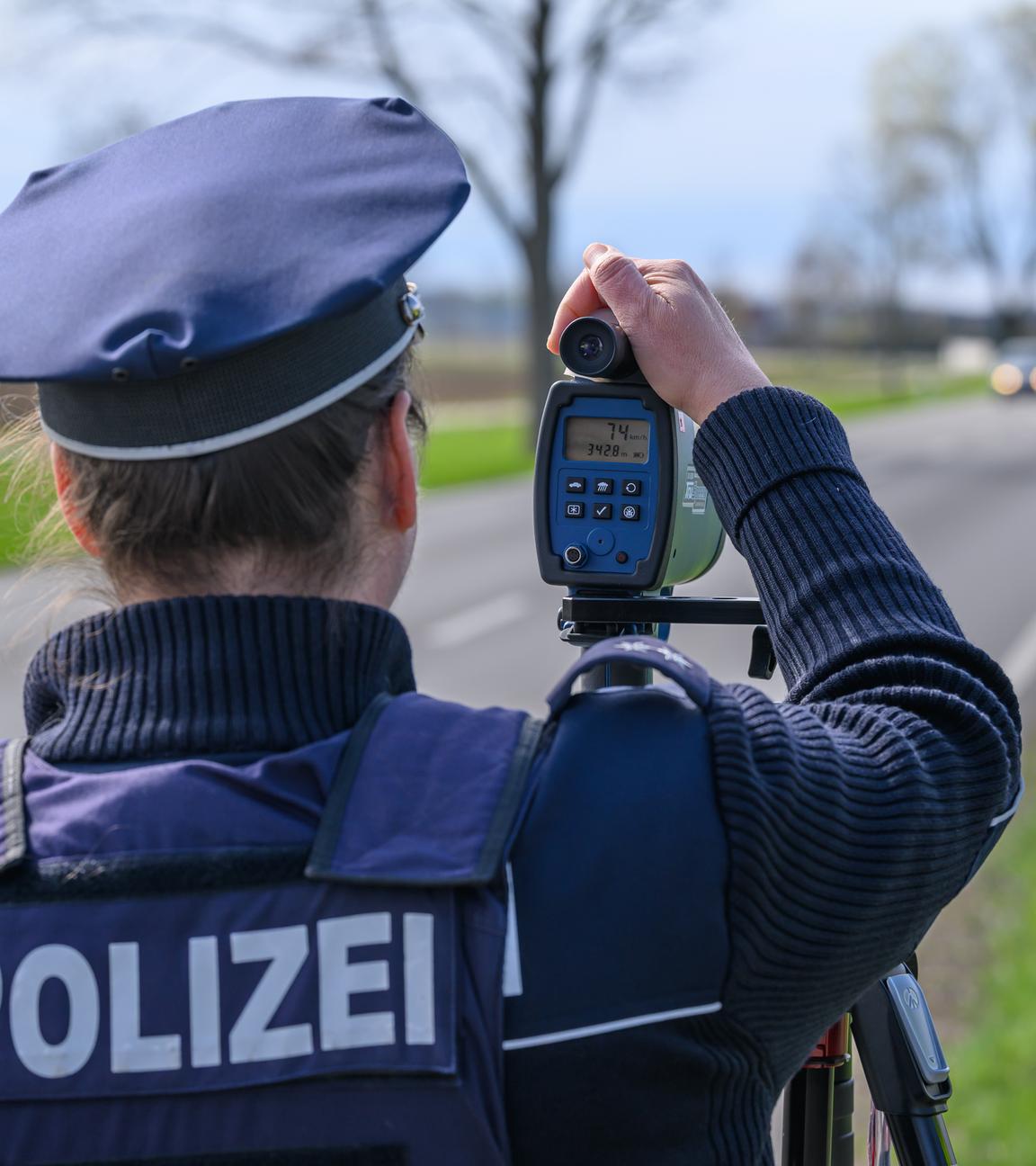 Eine Polizistin steht am Straßenrand und führt eine Geschwindigkeitskontrolle durch. 
