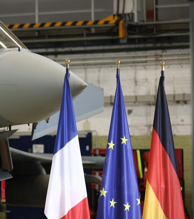 Die Flaggen von Frankreich, der EU und von Deutschland stehen vor einem Eurofighter. 