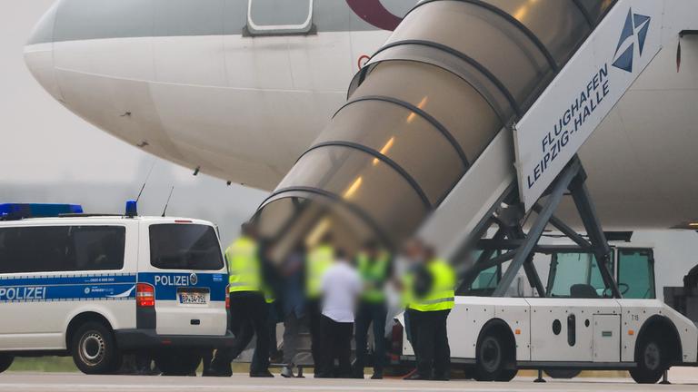 18.07.2025, Sachsen, Schkeuditz: Menschen besteigen ein Flugzeug der Qatar Airways, vor dem Fahrzeuge der Bundespolizei stehen auf dem Vorfeld am Flughafen Leipzig/Halle.