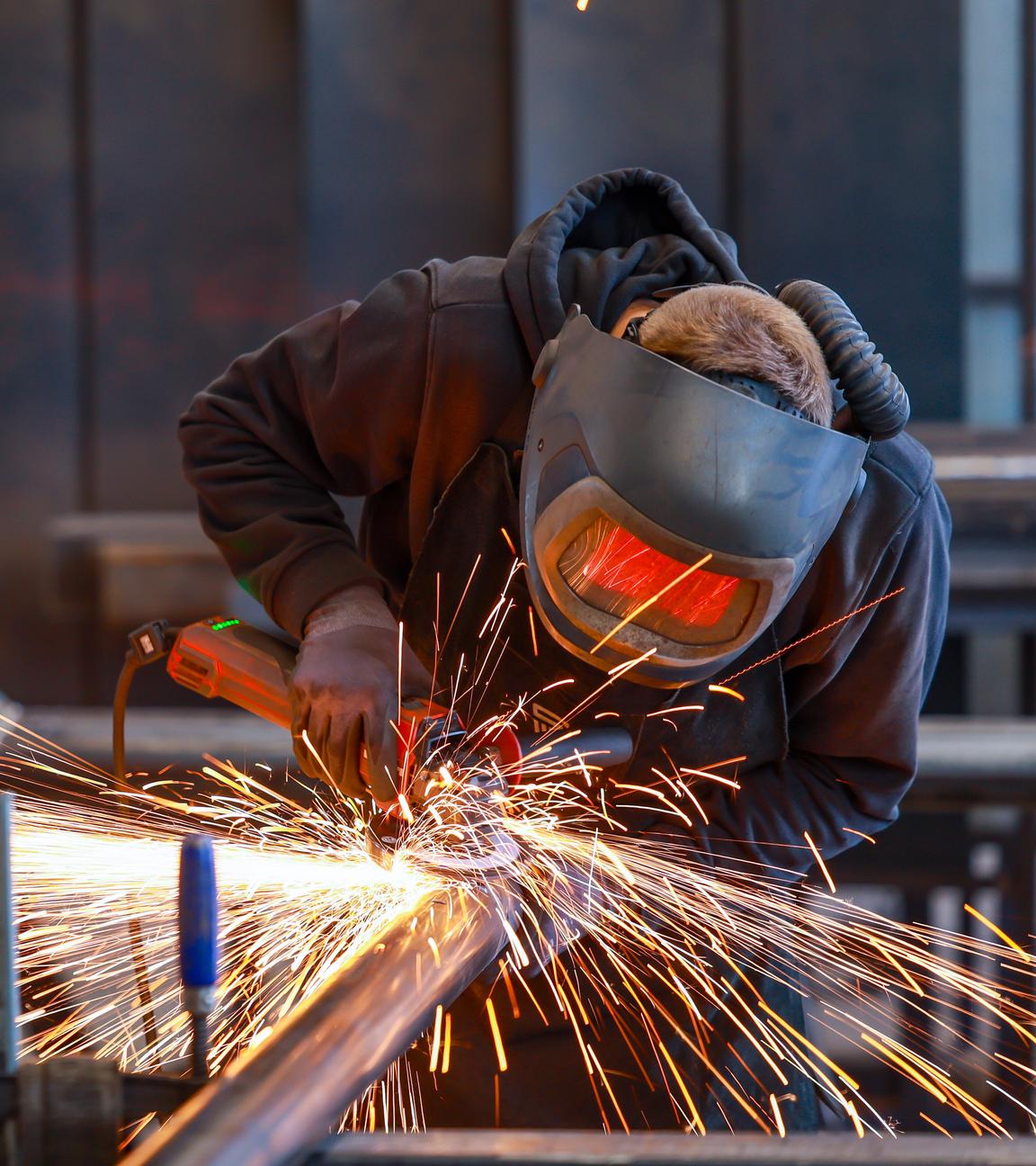Ein Industriearbeiter flext mit einem Winkelschleifer ein Stahlrohr
